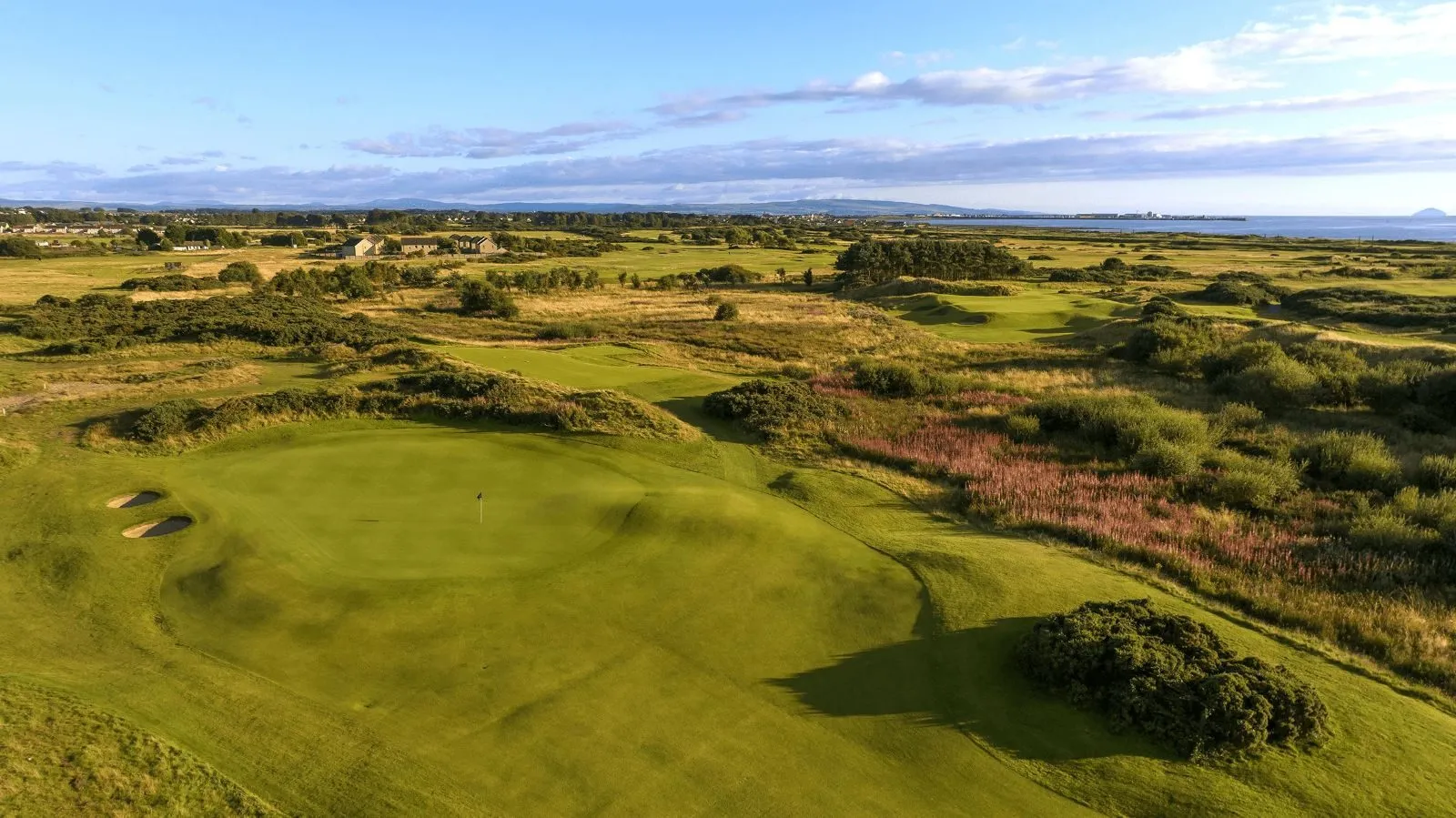 Aerial view of a links golf course green with bunkers, gorse and the sea beyond
